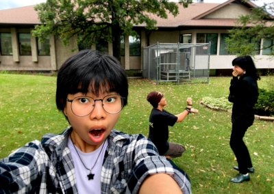 a photo of three friends, two of them proposing as a joke in the background whilst the third one is holding the camera looking shocked